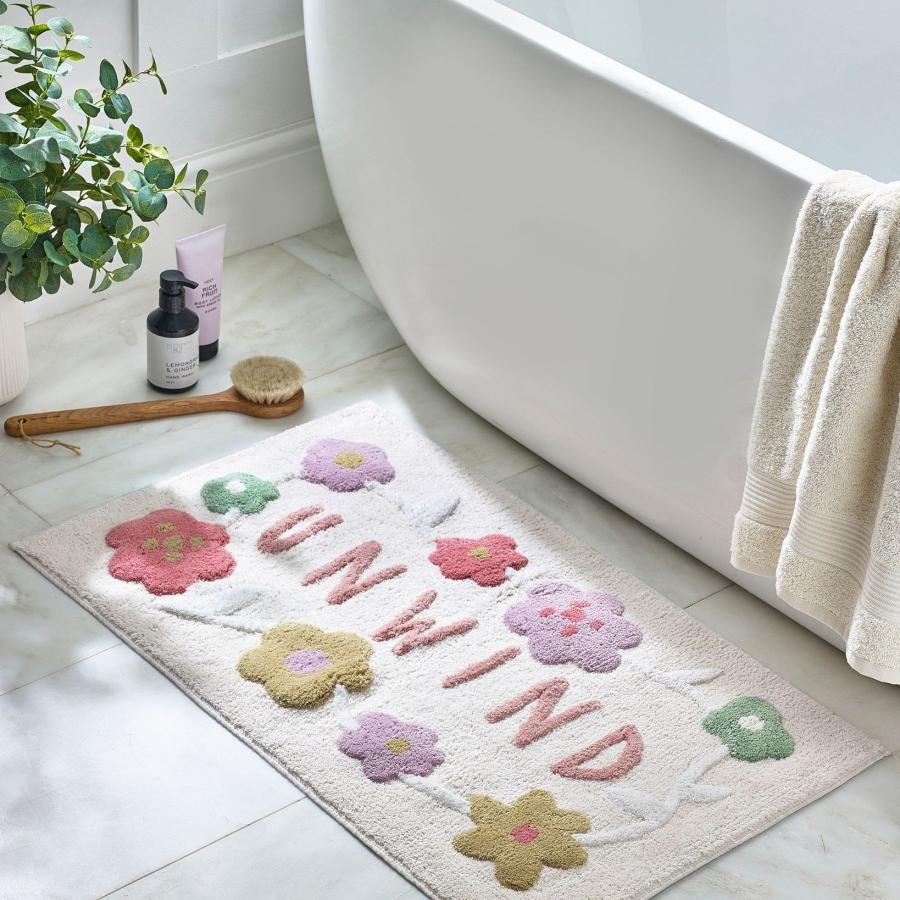 Floral bath mat with the word Unwind on it
