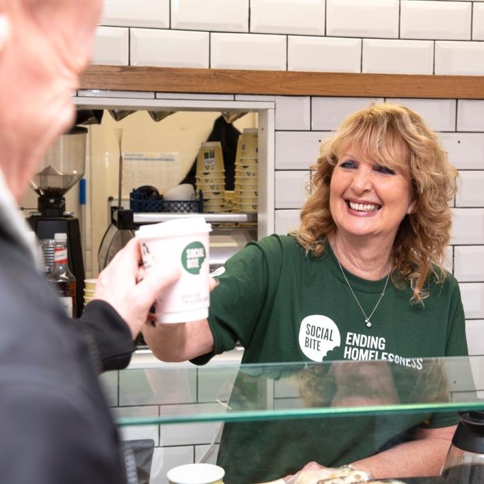 A volunteer at Social Bite handing over a coffee to a customer